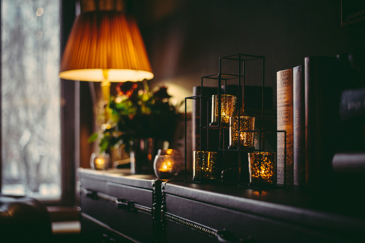 Warm amber candlelight and lamp glow on a dark editorial shelf